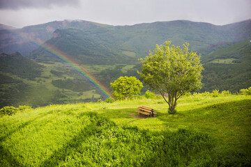 Rainbow over the mountains in Tatev, Syunik Province of Armenia. Mountain landscape in Armenia. Big green tree and the lonely bench next to the rainbow, Armenia