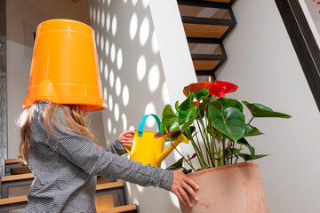 Little girl with bucket on her head takes care of the flowers of her home