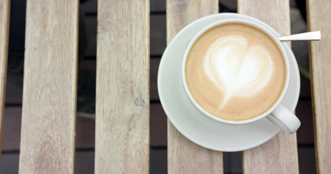 Overhead shot of cup of cappuccino being put down on wooden table