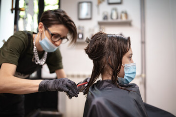 Fototapeta premium Hairdresser and girl child customer in a salon with medical masks during virus pandemic. Working with safety mask.