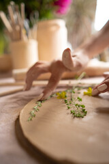 Closeup of hands potter master decorating the dishes at the workshop. Girl holding flowers in her hands. Ceramic workshop. Paint on clay mug in the pottery.