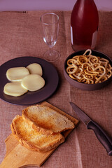 still life con aperitivo con pan tostado, queso, salados y vino rosado sobre mantel rustico