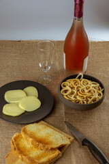 still life con aperitivo con pan tostado, queso, salados y vino rosado sobre mantel rustico