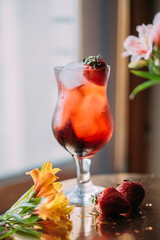 a red ingredient is added to the cocktail. cocktail with strawberries and ice on the background of a window and flowers

