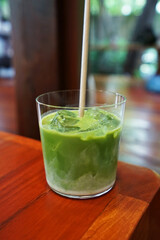 Close up glass of Iced Matcha green tea latte on wooden tray table