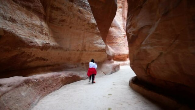 Tilt down shot of woman walking in alley amidst rock formations - Petra, Jordan