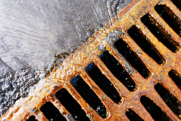Gutter drain. Storm sewage during rain. Rusty, steel drain cover