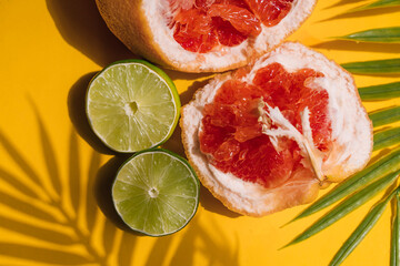 broken grapefruit with sliced ​​lime on a yellow background with green leaves