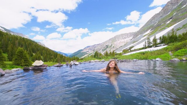 Handheld view of woman swimming inside hot springs on Conundrum Creek Trail in Aspen, Colorado in 2019 summer with view of mountains