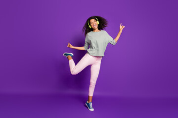 Full size photo of crazy cheerful teenager afro american girl listen song use headset sing dance feel rejoice scream wear striped shirt pink pants trousers isolated over purple color background