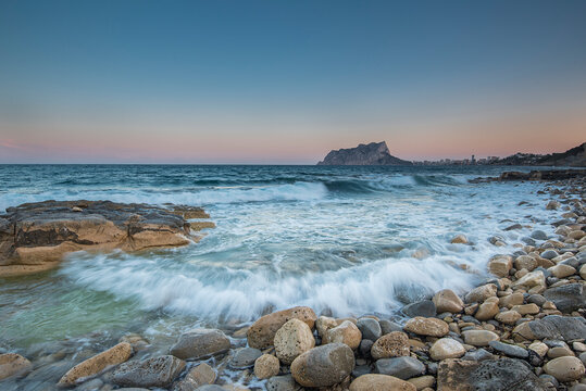 Paisaje del pe&ntilde;&oacute;n de Ifach desde la cala de Baladrar en Benissa, con ola rompiendo en primer plano, rocas y de fondo el pe&ntilde;&oacute;n de Ifach