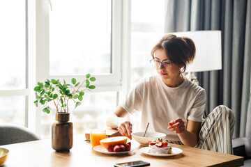 Photo of woman eating fruits and pancakes while having breakfast