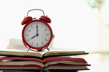 Red alarm clock standing on pale of books