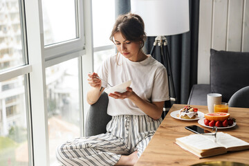 Photo of young cute woman having breakfast while sitting at table