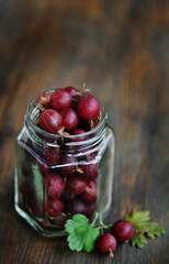 Fototapeta na wymiar Red gooseberry in a glass jar on an old wooden background. Canning of berries. Planned to make jam from gooseberry. Soft focus. Place for text.copy space 