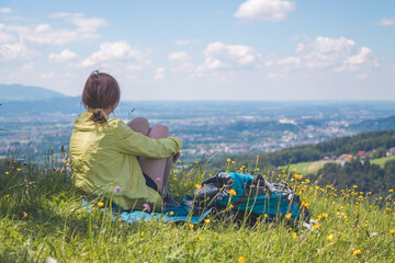 Enjoying the idyllic mountain landscape: Girl is sitting on idyllic meadow and enjoying the view over the far away city of Salzburg