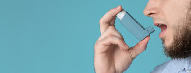 Closeup view of man using asthma inhaler on blue background, space for text. Banner design