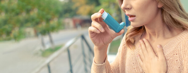 Closeup view of woman using asthma inhaler outdoors, space for text. Banner design