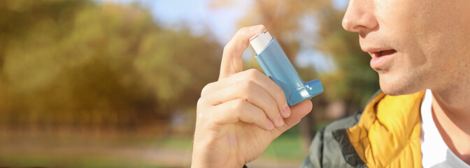 Closeup view of man using asthma inhaler outdoors, space for text. Banner design