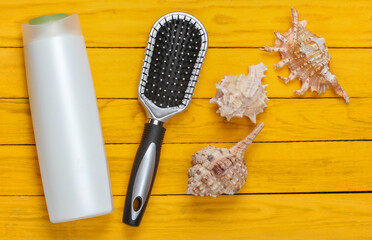 Shampoo bottle with comb and shells on a yellow wooden background. Top view