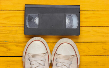 Retro sneakers from the 80s and video cassette on yellow wooden background. Top view