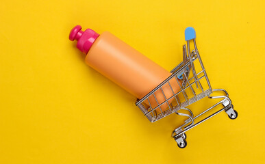 Mini supermarket trolley with shampoo bottle on a yellow background. Top view