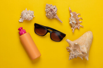 Obraz premium Bottle of sunblock with sunglasses, seashells on a yellow background. Beach Vacation Concept. Top view