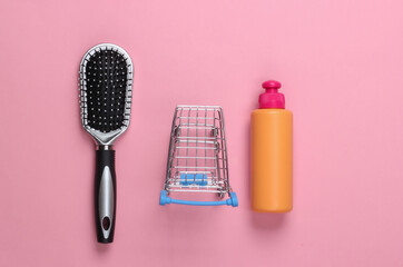 Shampoo bottle, hairbrush with mini supermarket trolley on pink pastel background. Shopping. Beauty and hair care. Top view. Minimalism