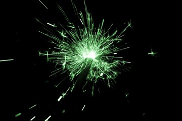 Green sparkler countdown on fire with spread of glitter sparks. Luxury entertainment at e.g. New Years Eve, Independence Day or birthday party celebration. Glowing light spark on dark background