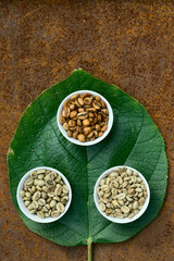  Flat lay  of   brown and green coffee beans in ceramic bowl, green leaf on   beans of coffee