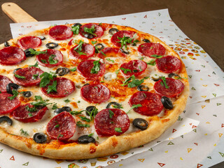 Large pizza with salami and olives sprinkled with chopped herbs closeup