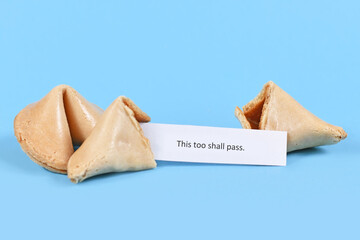 Broken up and whole fortune cookie with motivational text 'This too shall pass' on paper note on...