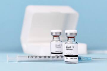 Coronavirus vaccine concept with two small vial bottles with text 'Covid-19 vaccine' with syringe and storage case in blurry blue background