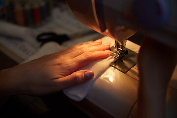A woman sews a protective mask from viruses on a sewing machine. 
