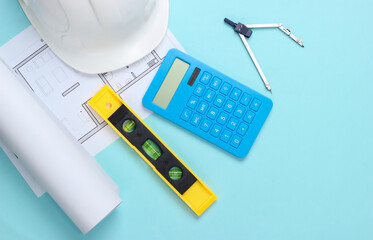 Hard hat with building level, calculator, compass, blueprint on blue studio background. Engineering, construction equipment. Top view