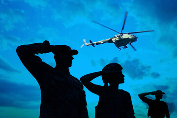 Silhouettes of soldiers in uniform saluting and military helicopter outdoors