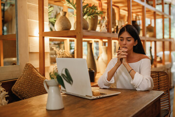 Focused young  caucasia woman sitting alone at a counter in a cafe working on a laptop, thinking about new online project. Freelancer girl work with laptop