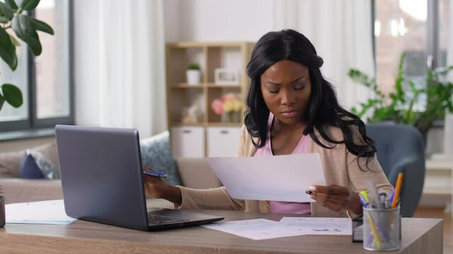 remote job, technology and people concept - stressed young african american woman with laptop computer and papers working at home office