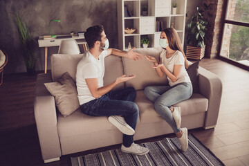 Obraz premium Photo of young couple two people lady guy students spend quarantine together stay home talking have fun good mood sit sofa divan wear facial medical mask room indoors