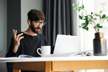 Image of nervous man using wireless earphones and working with laptop