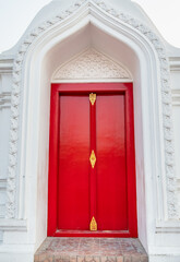 Red wooden temple doors With a white concrete arch Is a unique temple in Thailand.