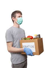 volunteer in medicine mask, protective gloves holding grocery food in carton donation box: vegetable oil, grape, tin cans, tomatoes. Coronavirus relief funds, charity help, delivery, local support