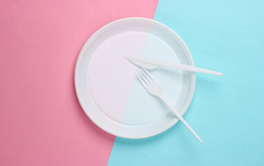 Plastic plate with fork and knife on pink blue background. Picnic. Plastic pollution. Top view