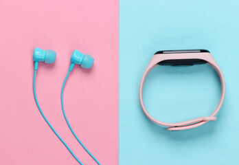 Earphones with smart bracelet on pink blue pastel background. Modern gadgets. Top view