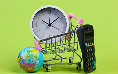 School supplies with a sopping trolley on green background. Shopping cart, globe, calculator, clock. Shopping time