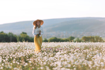 Beautiful girl in a yellow dress on a field of daisy flowers.