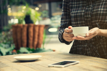 Woman holding a cup of coffee with smartphone on the table outdoor cafe.