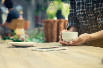 Woman holding a cup of coffee with smartphone on the table outdoor cafe.
