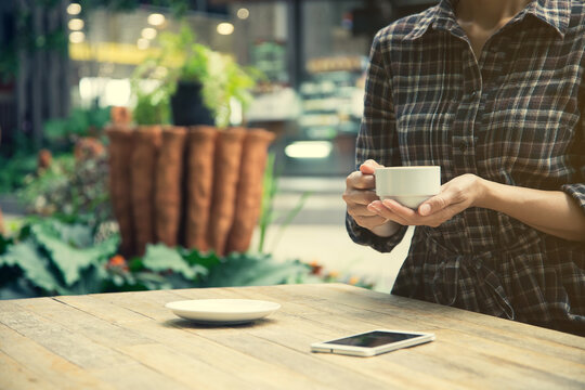 Woman holding a cup of coffee with smartphone on the table outdoor cafe.