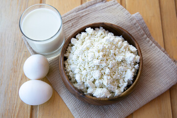cottage cheese on wooden plate , egg and glass milk on a brown towel and a wooden table
